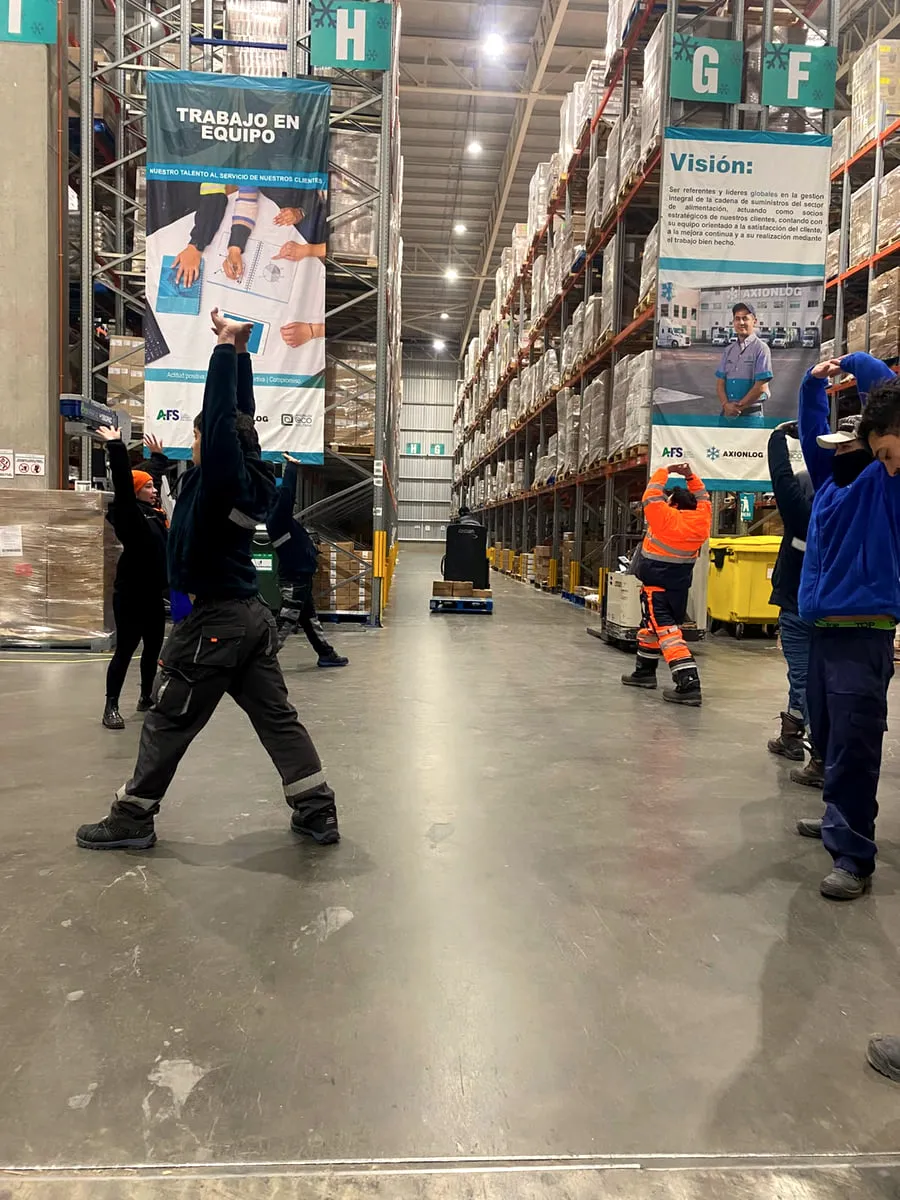 Trabajadores de Axionlog siguiendo técnicas de estiramiento de pie en su lugar de trabajo.