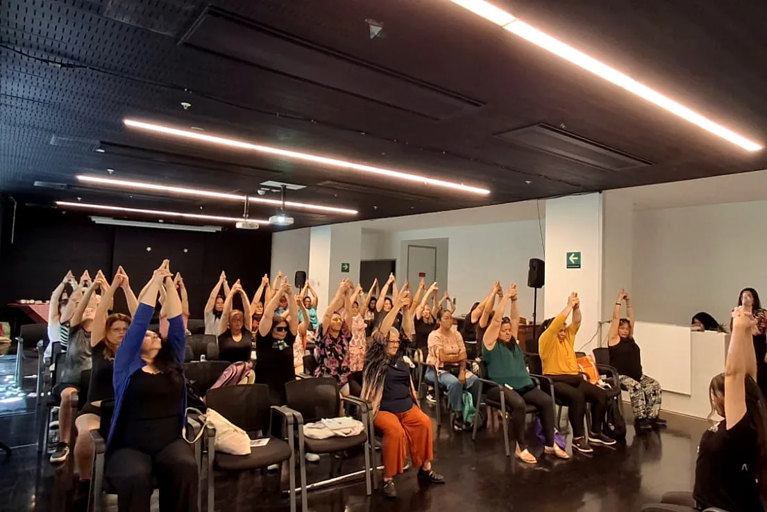 Alrededor de treinta personas sentadas en sillas en el Hospital Félix Bulnes, estirando ambos brazos hacia arriba al mismo tiempo durante una pausa activa.